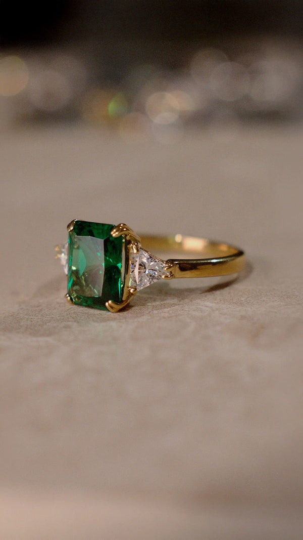 Gold ring for women with a radiant cut emerald and sparkling triangle cut shoulder stones.