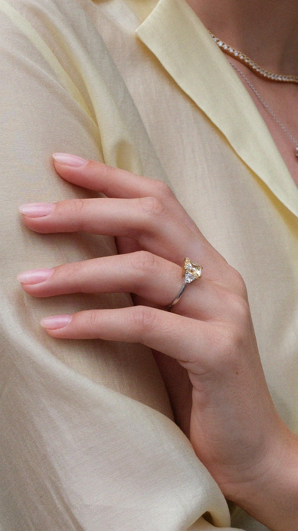 Hand wearing a trilogy ring with light yellow princess cut gemstone and sparkling side stones on a sterling silver band.