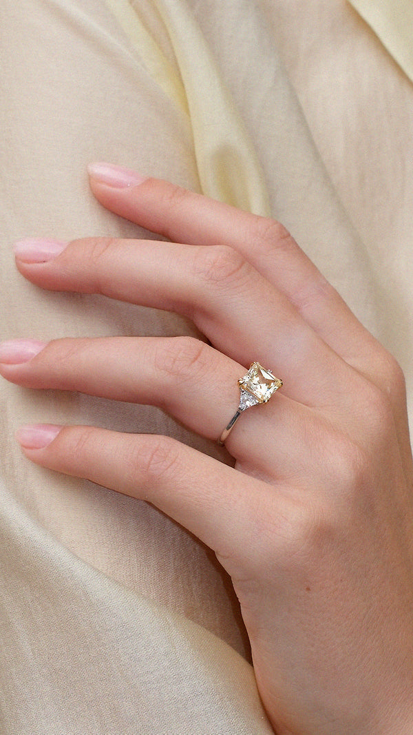 Hand wearing a light yellow diamond style trilogy ring with sparkling side stones on a sterling silver band.