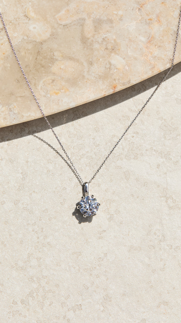 Solid white gold necklace with a pendant on a beige stone surface.