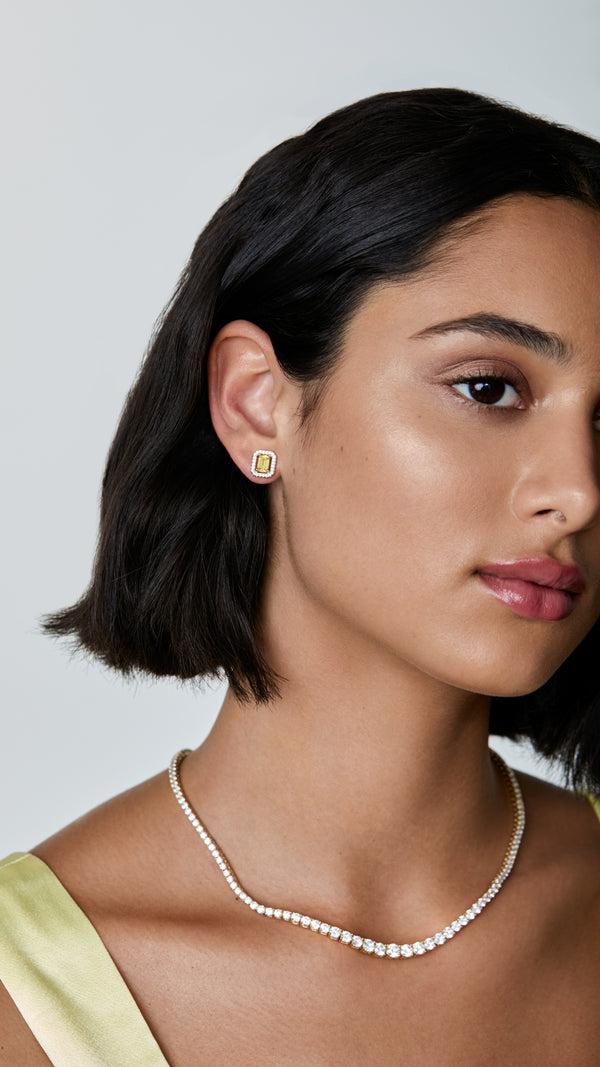 Woman wearing a statement tennis necklace and with emerald cut stud earrings.