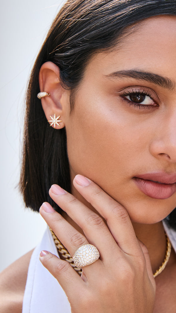 Close-up of a woman wearing gold earrings and a ring on a plain background