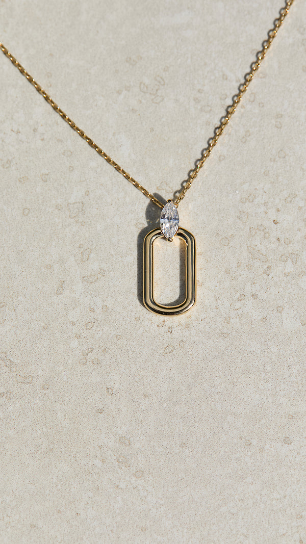Gold necklace with a marquise stone unique pendant on a light gray background