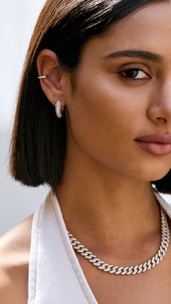 Close-up of a woman wearing silver hoop earrings and a cuban chain necklace with pave detailing