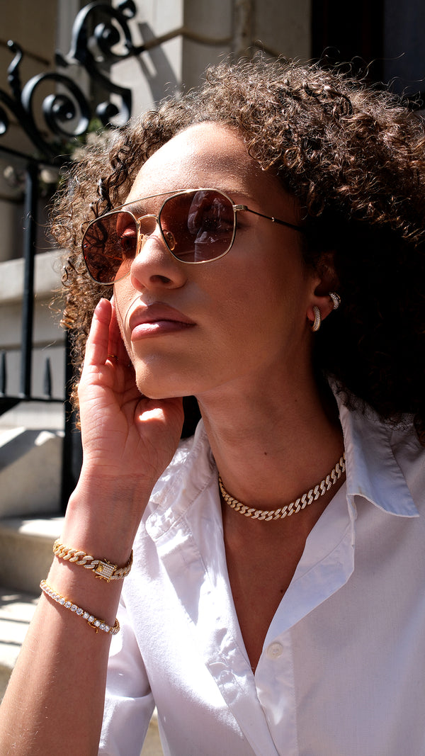Woman wearing a white shirt with stacked gold jewellery. Gold cuban chain neclace paired with a gold tennis bracelet.
