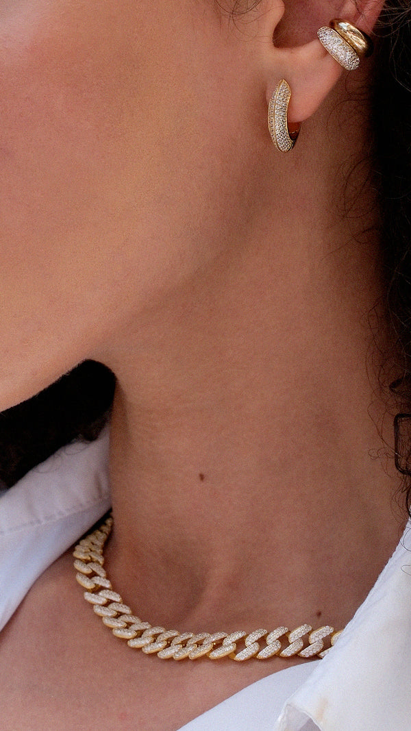 Close-up of stacked gold hoop earrings and a gold cuban chain necklace on a woman wearing a white shirt.