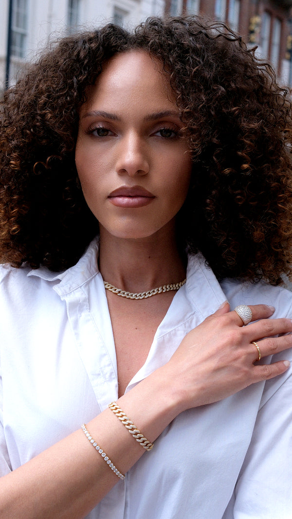 Woman wearing gold cuban chain neclace with chunky gold bracelet and tennis bracelet and domed gold ring.