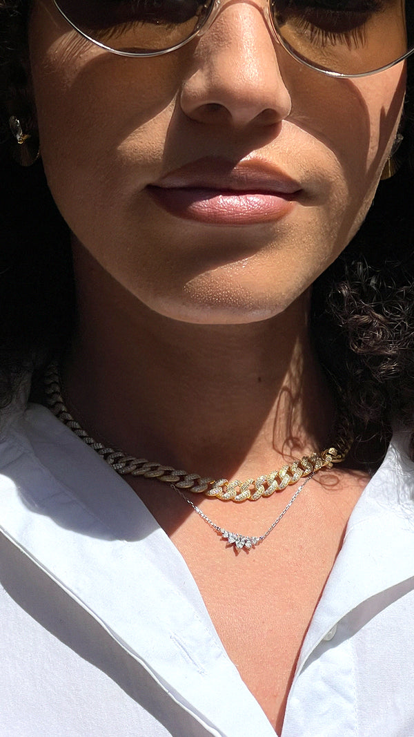 Close-up of a women with layered necklaces with a white shirt. One necklace is a gold cuban chain the other a sterling silver delicate gemstone necklace.
