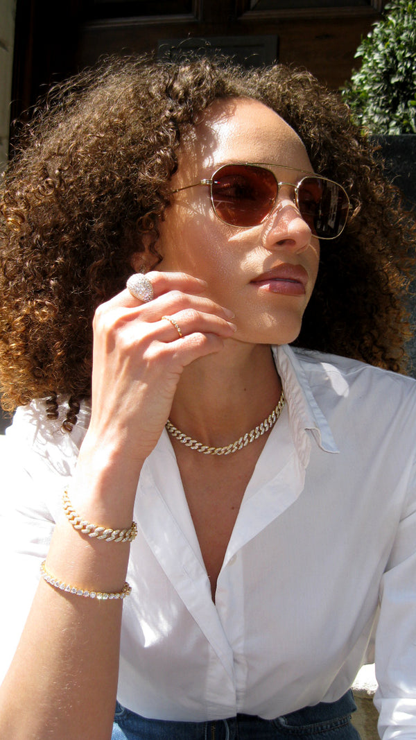 Woman with gold tennis bracelet stacked with a gold cuban chain bracelet and cuban chain gold chunky necklace.
