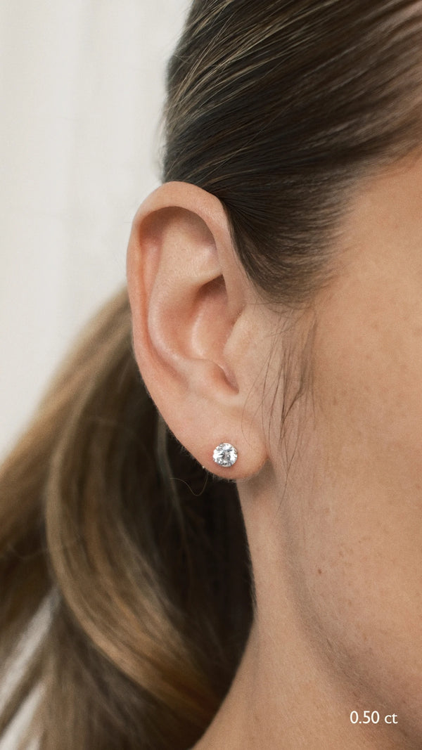 Close-up of a model wearing everyday 0.50 carat round brilliant solitaire stud earrings in 9K white gold, demonstrating the secure, flush fit on the earlobe.
