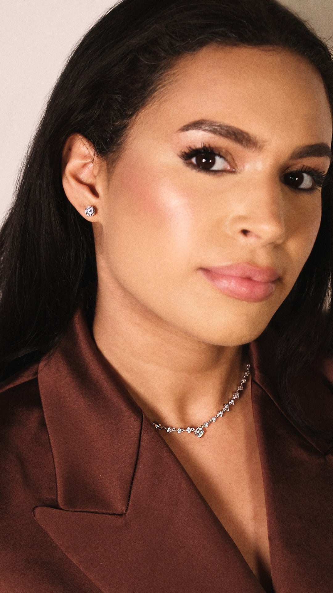 Woman wearing a brown satin jacket with a close-up of 1ct stud earrings.