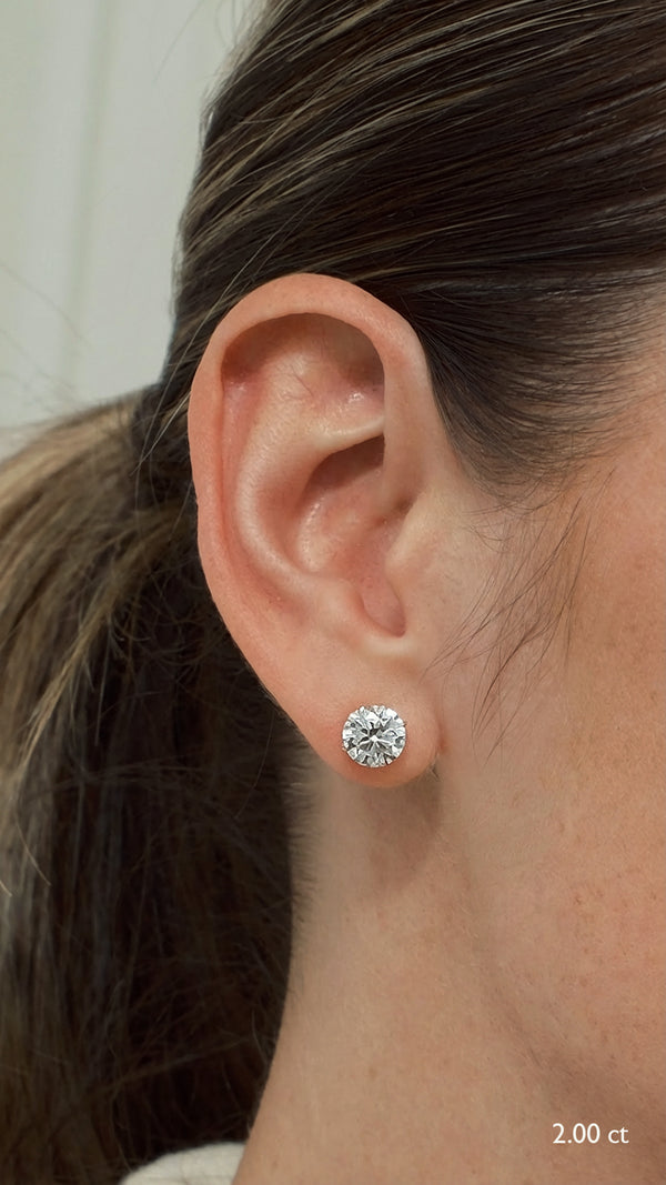 Side profile of a model's ear wearing statement 2.00 carat round brilliant solitaire stud earrings in 9K yellow gold, showing how the tapered basket sits flush against the skin.