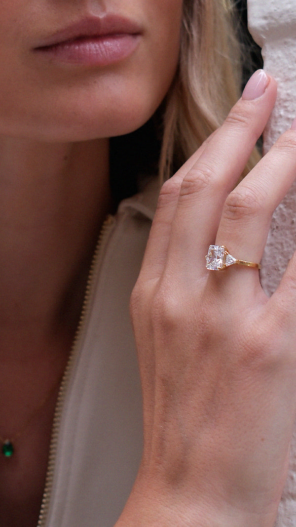 Close-up of a hand wearing a diamond style trilogy ring with sparkling side stones.