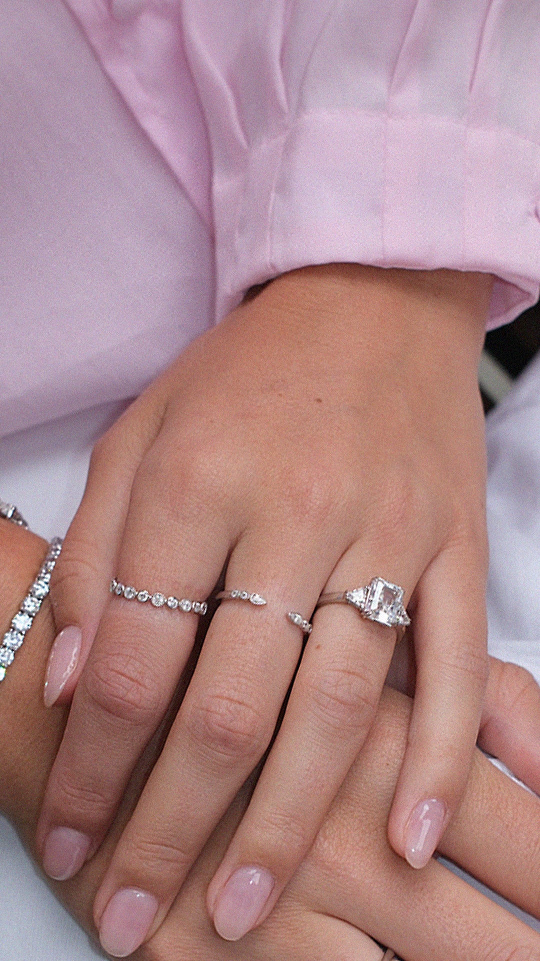 Close-up of a hand wearing multiple sterling silver stacking rings styled with a sterling silver radiant cut trilogy ring. 