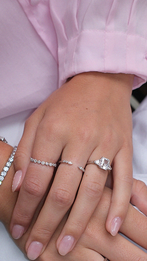 Close-up of a hand wearing multiple sterling silver stacking rings styled with a sterling silver radiant cut trilogy ring. 