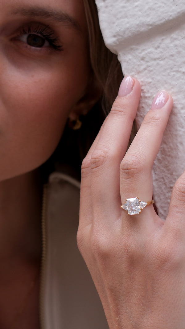 Close-up of a hand wearing a diamond style trilogy gold ring with a blurred background