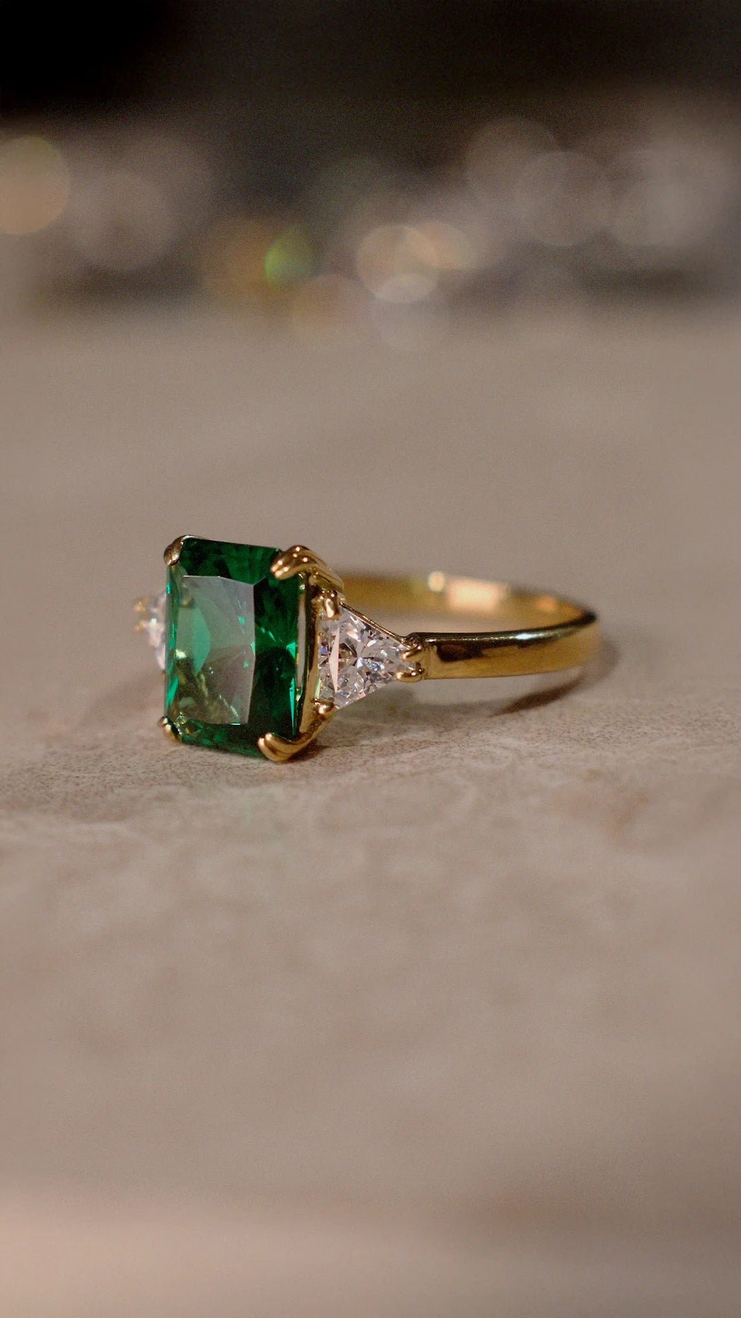 Gold ring for women with a radiant cut emerald and sparkling triangle cut shoulder stones.