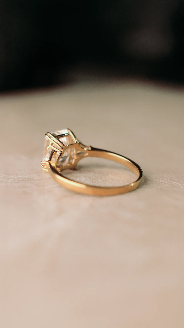 Gold ring with a radiant cut gemstone on a beige surface