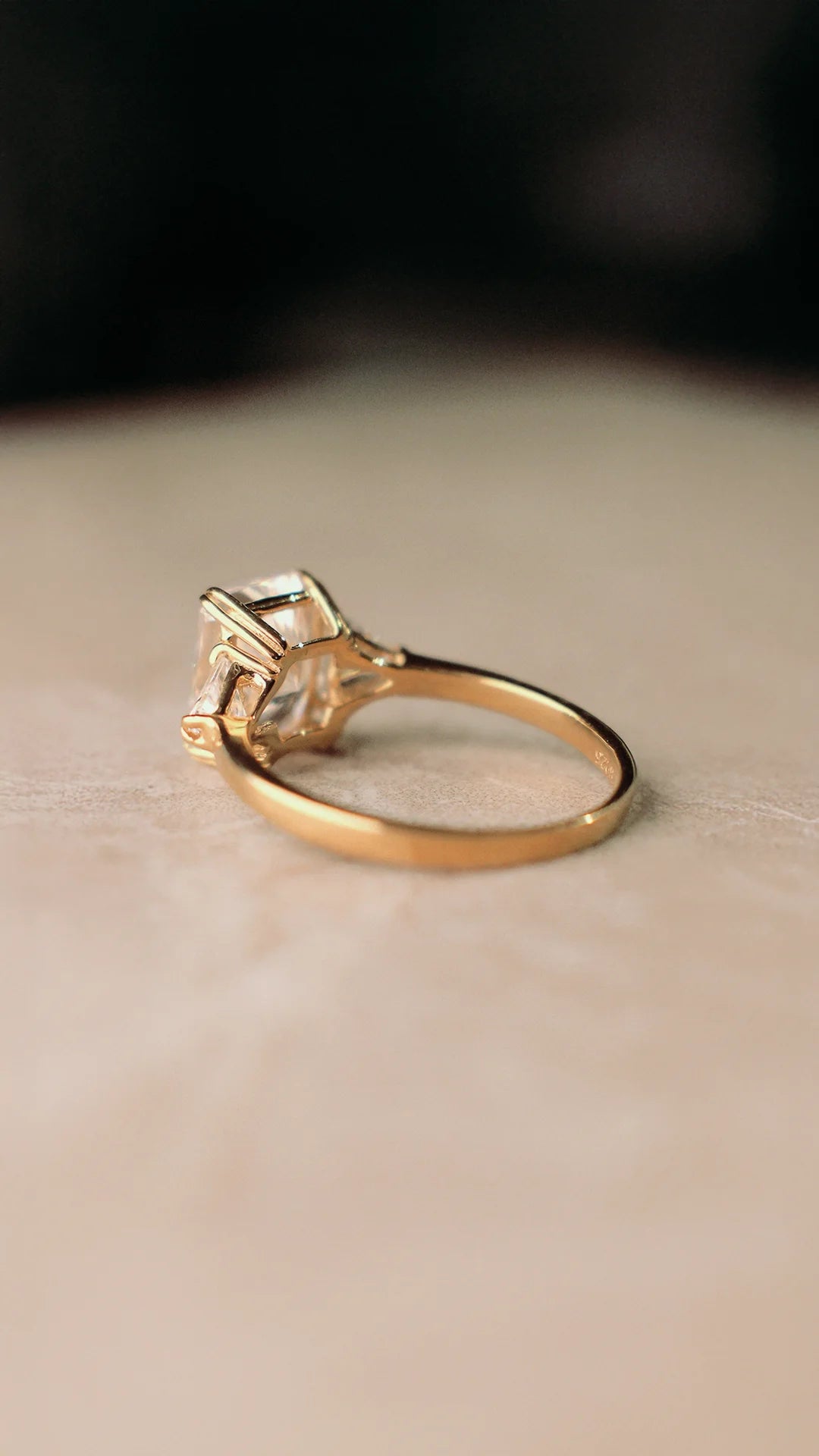 Gold ring with a radiant cut gemstone on a beige surface