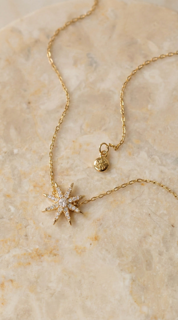 Gold necklace with a star-shaped pendant on a beige marble surface