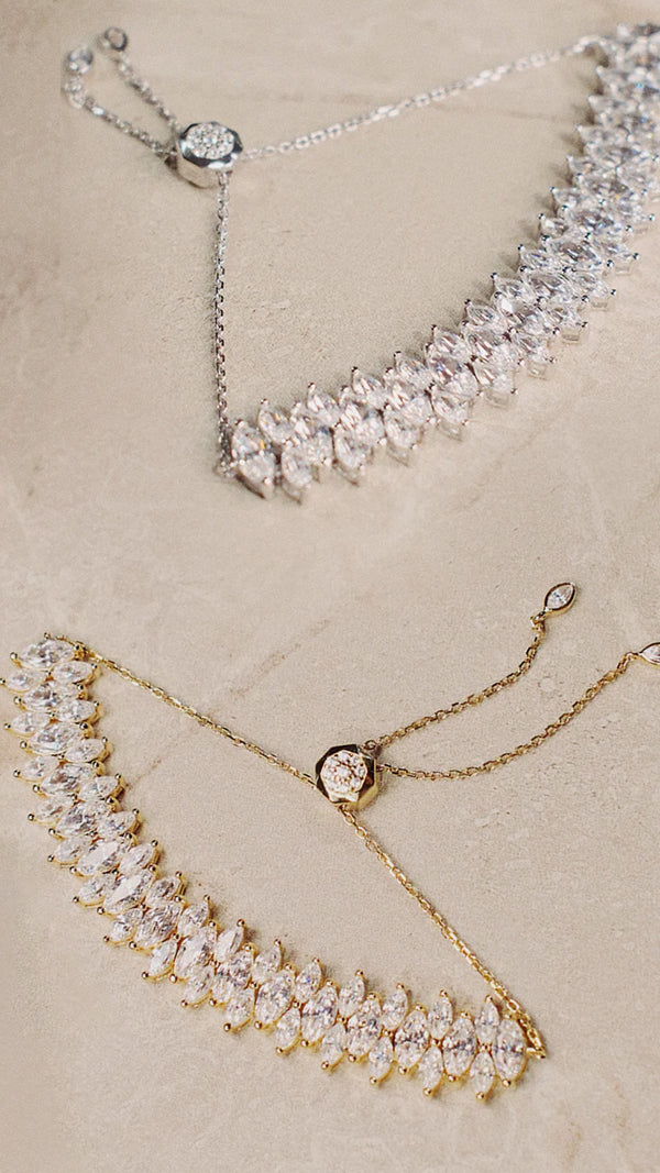 Two gold and silver necklaces with crystal-like stones on a beige background