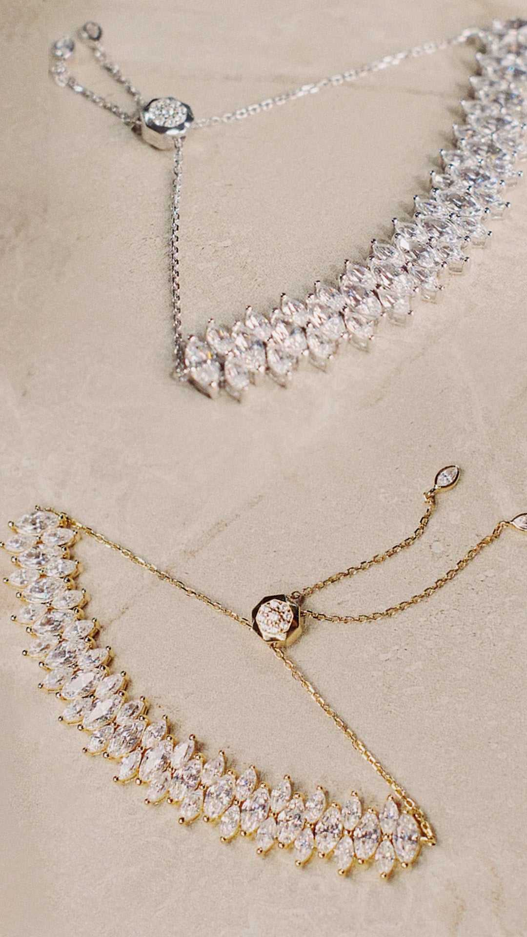 Two gold and silver necklaces with crystal-like stones on a beige background