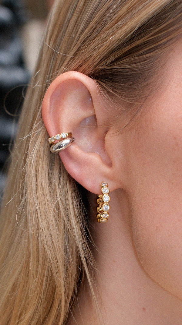 Close-up of an ear with gold hoop earrings and a gold and silver mixed metal ear cuff stack.