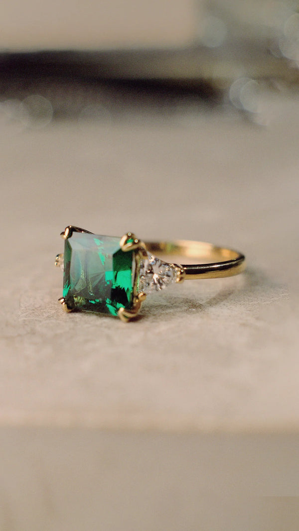 Gold ring with an emerald princess-cut gemstone and triangle shoulder stones. 