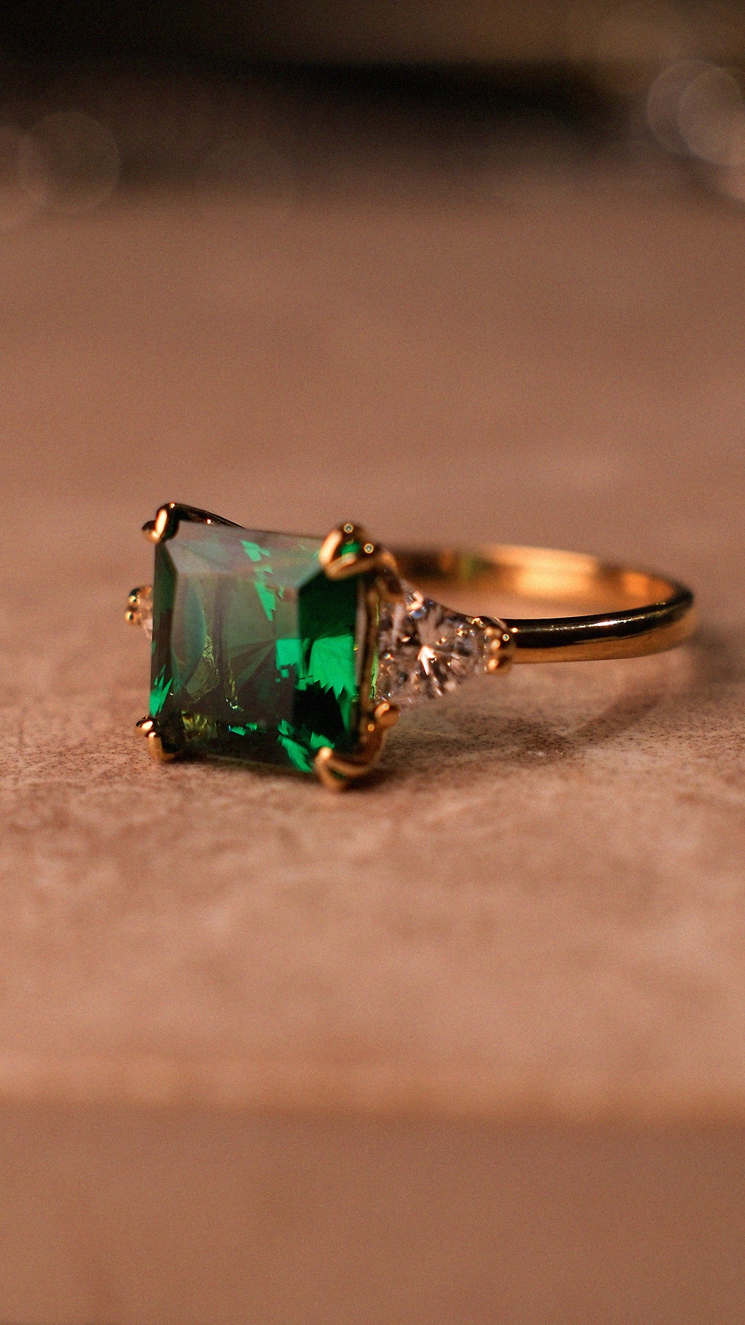 Gold ring with an emerald princess-cut gemstone and triangle shoulder stones. 