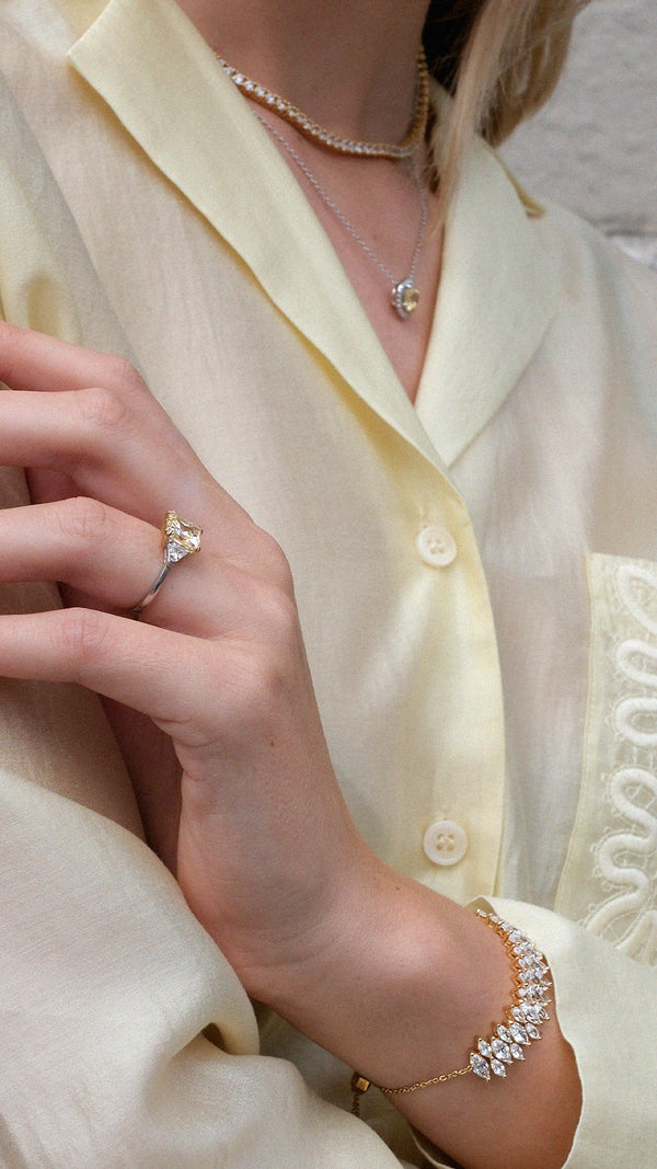 Close-up of a person wearing a yellow gemstone ring, necklace, and gold diamond style marquise tennis bracelet. 
