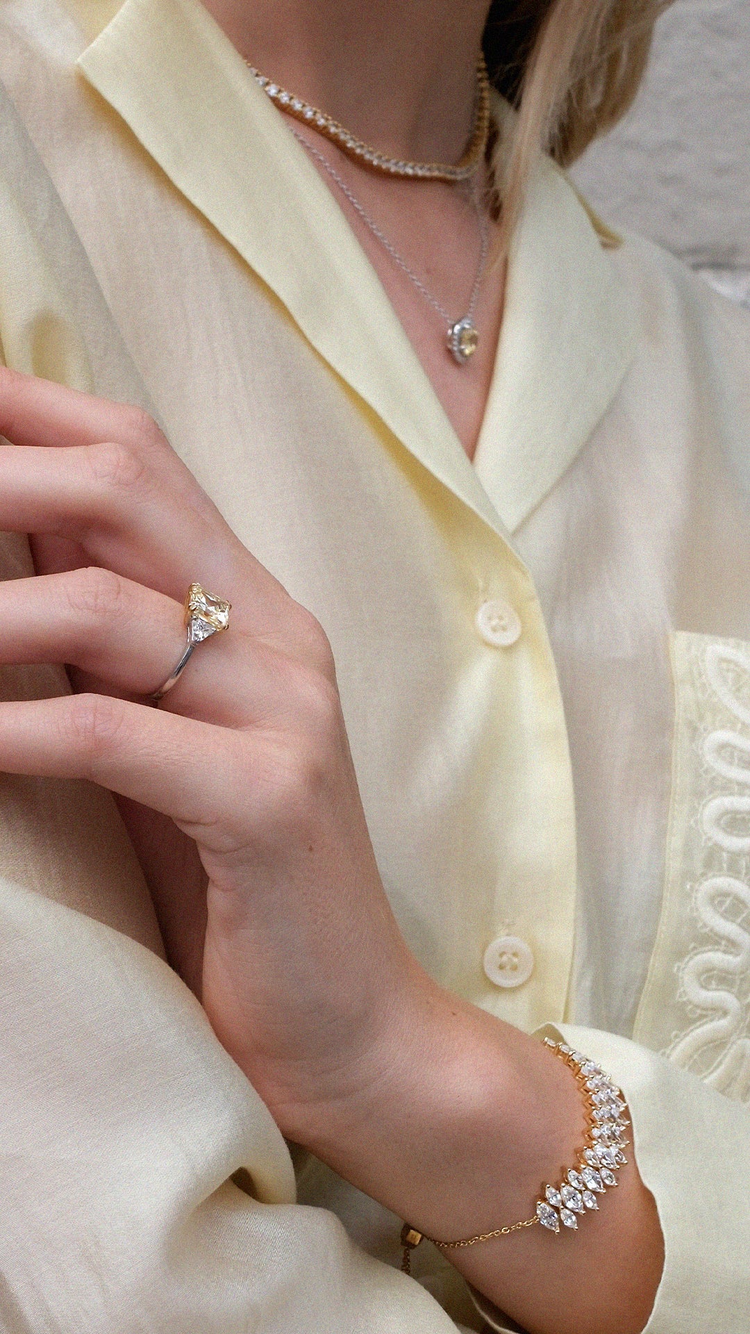 Close-up of a person wearing a yellow gemstone ring, necklace, and gold diamond style marquise tennis bracelet. 