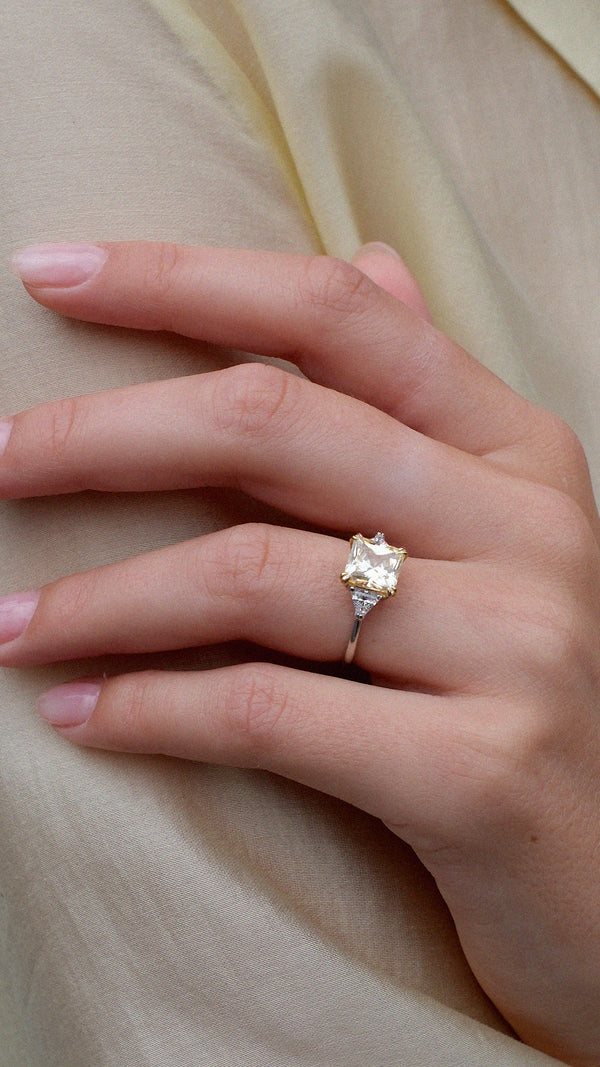 Hand wearing a sterling silver trilogy ring with a light yellow princess cut gemstone.