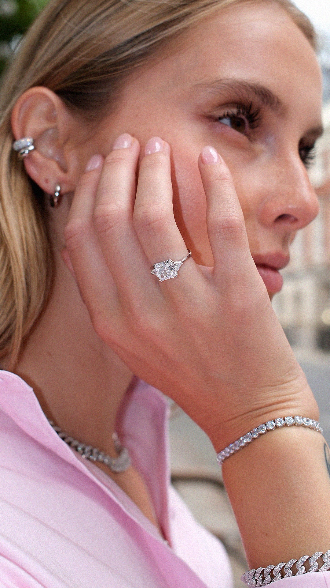 Close-up of a woman wearing diamond style sterling silver trilogy ring with a tennis bracelet and silver ear stack. 