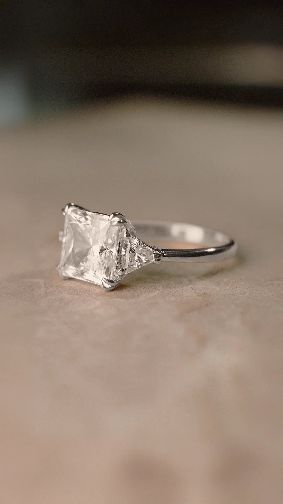 Sterling silver trilogy ring with a large princess-cut diamond style gemstone on a beige background.