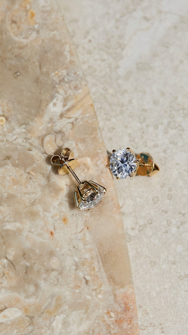 6 prong lab grown diamond studs set in yellow gold on a marble surface.