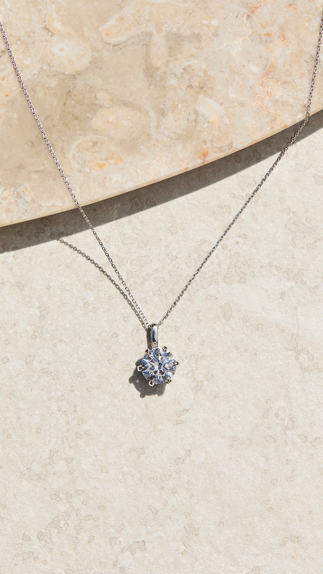 Solid white gold necklace with a pendant on a beige stone surface.