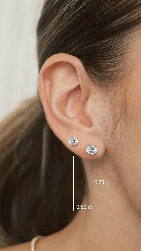Close-up of an ear wearing two diamond style 0.75ct and 0.50ct stud earrings with size labels.