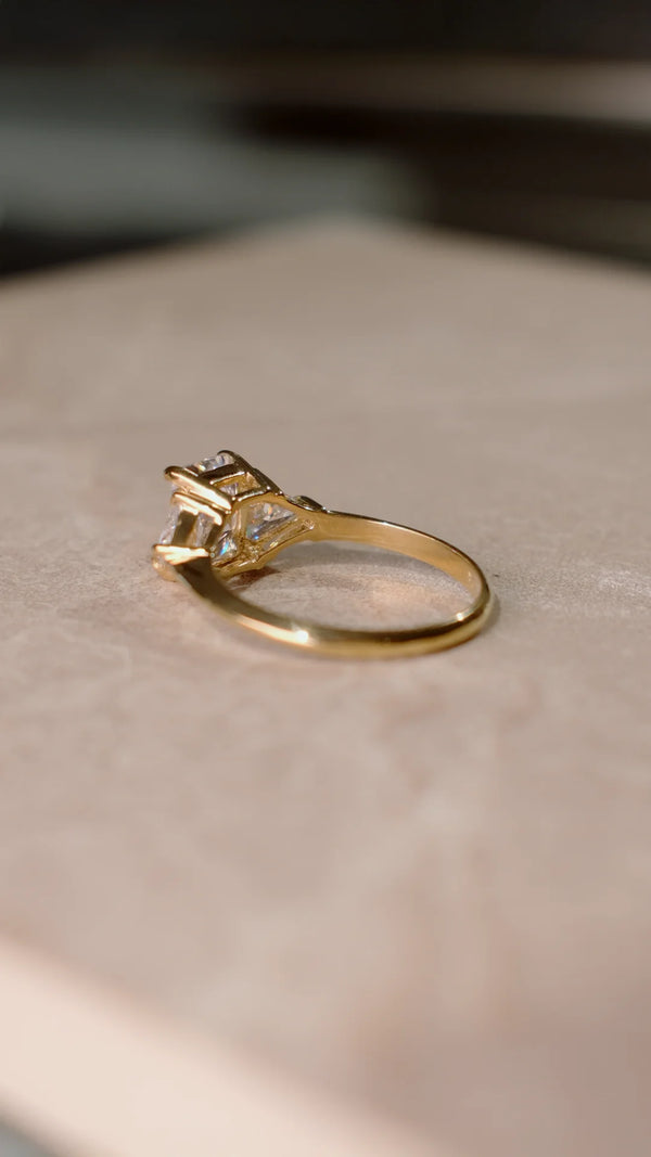Gold ring with a diamond style radiant cut gemstone on a beige surface.