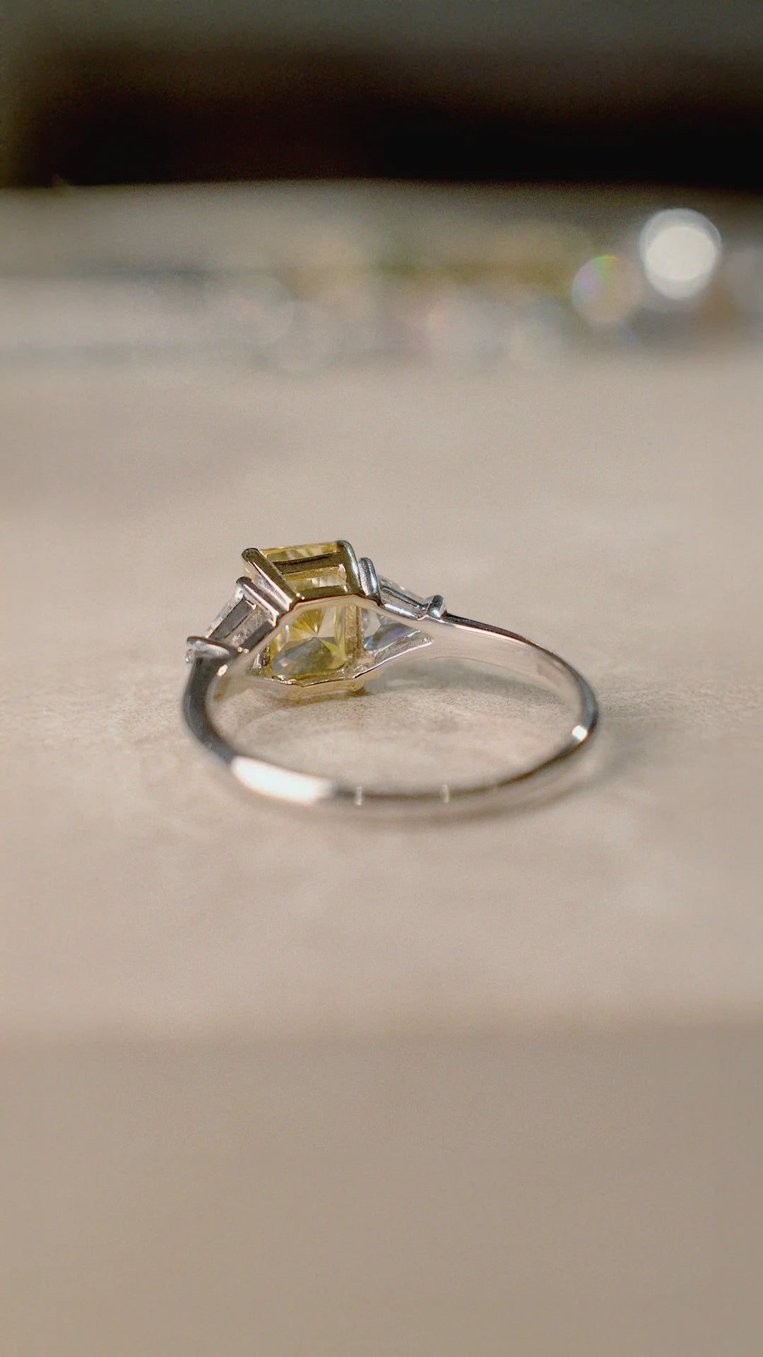 Silver trilogy ring with a yellow gemstone and triangular side stones on a beige surface.