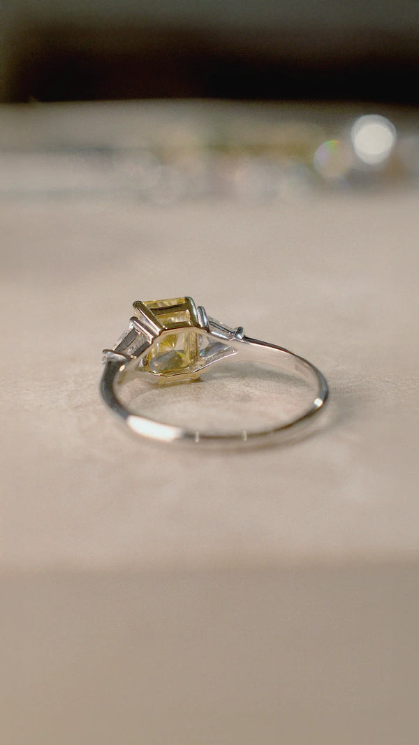 Silver trilogy ring with a yellow gemstone and triangular side stones on a beige surface.