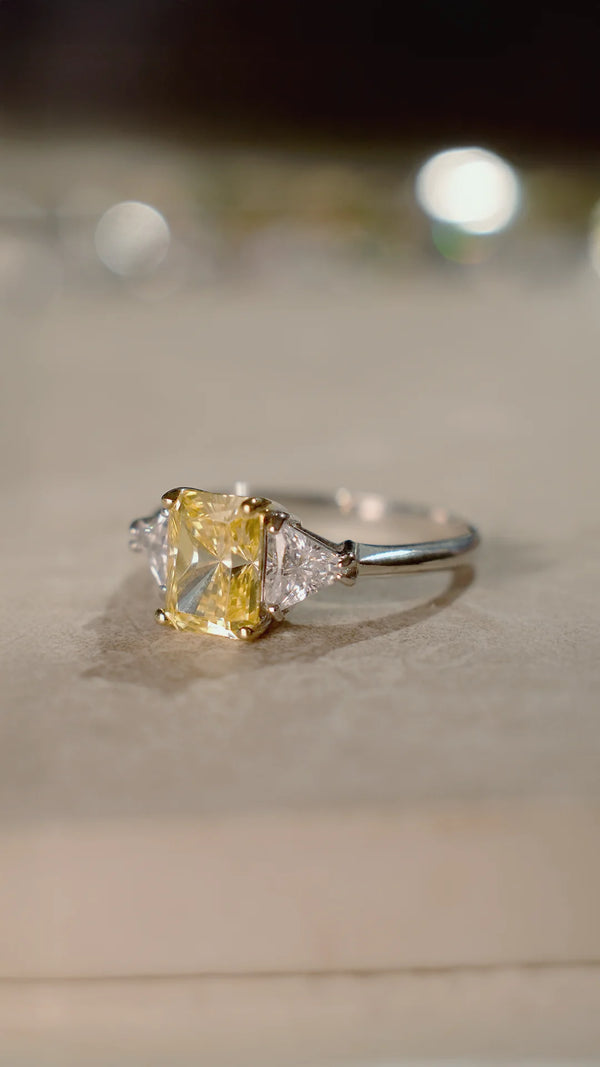 Ring with a light yellow radiant cut gemstone complemented by trillion-cut side stones.