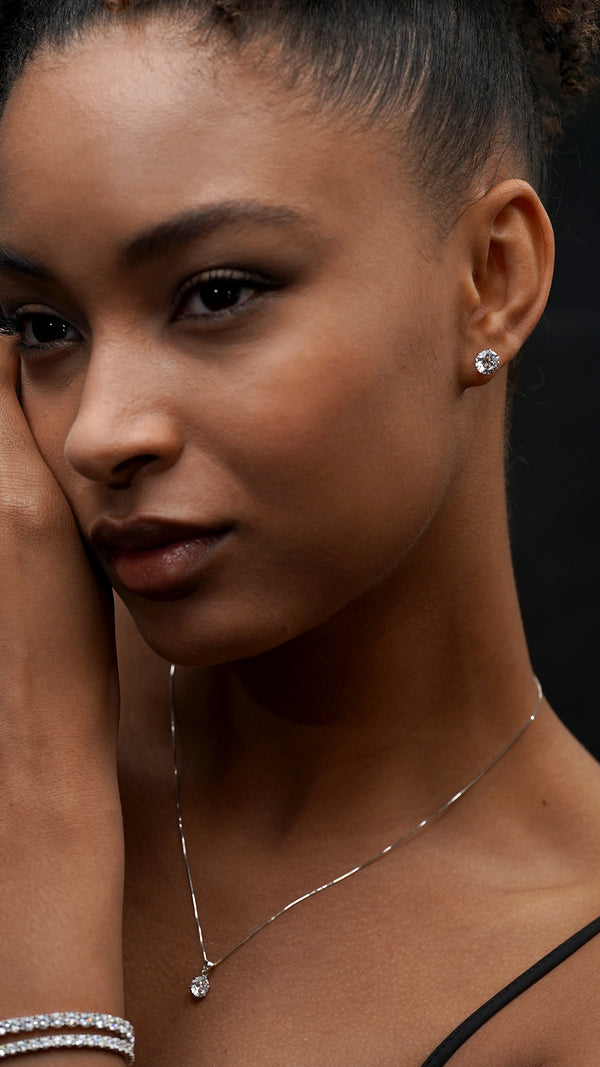 Brilliant cut solitaire stud earring in a 9K white gold setting on ear with layered tennis bracelets. 