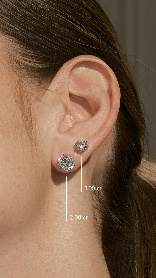 Close-up of an ear wearing 1ct and 2ct stud earrings with size labels.