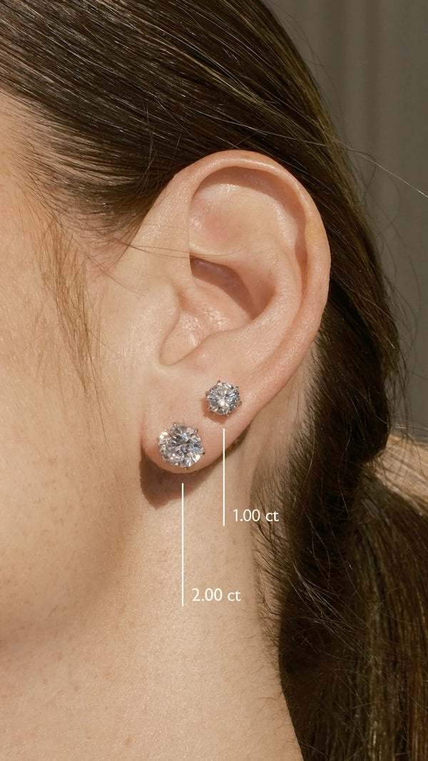 Close-up of an ear wearing 1ct and 2ct stud earrings with size labels.