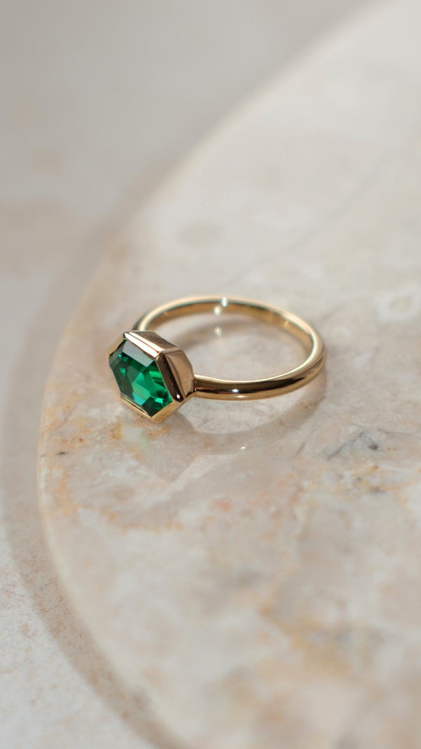 Gold ring with a lab-grown emerald green gemstone on a marble surface