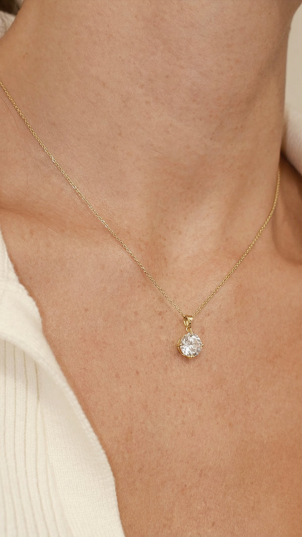 Gold necklace with a 2ct diamond style pendant on a person's neck