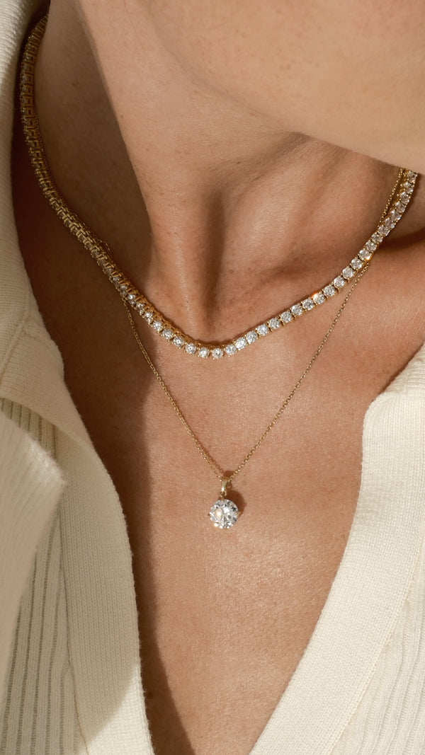 Close-up of a person wearing a gold tennis necklace layered with a gold pendant necklace.