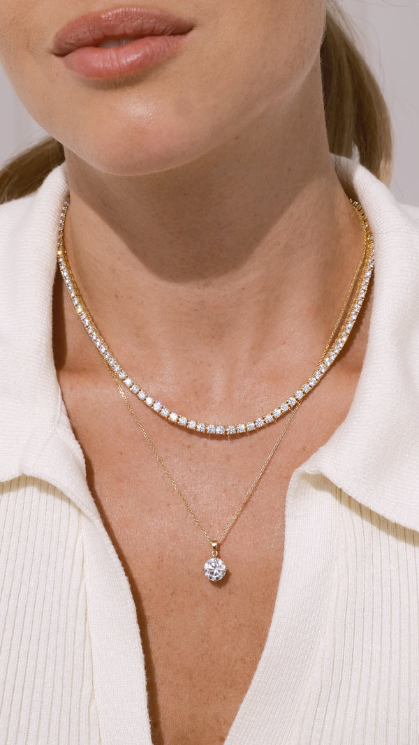 Close-up of a person wearing a 9k solid yellow gold necklace with a 1ct pendant paired with a gold vermeil classic tennis necklace.