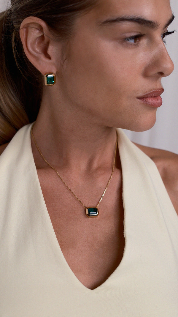 Woman wearing the gold Lily necklace with a green gemstone pendant with matching chunky emerald green and gold earrings.