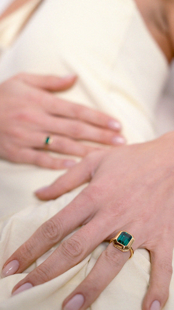 Close-up of hands wearing rings with green gemstones paired with a light yellow dress.